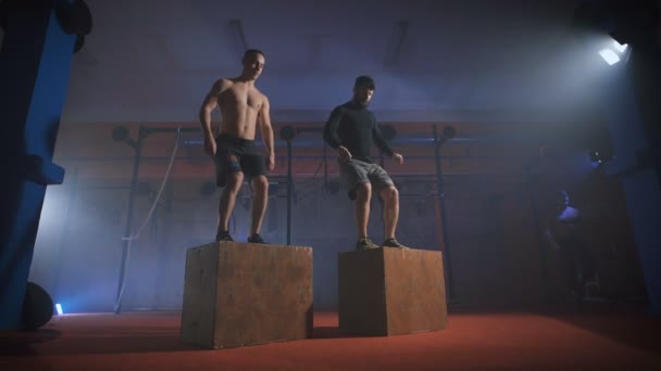 Dos hombres haciendo un salto de caja en el gimnasio . — Vídeo de stock