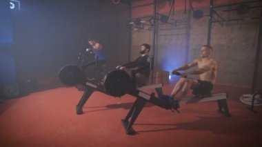 Üç genç sporcu eğitim cihazları üzerinde yapıyor.