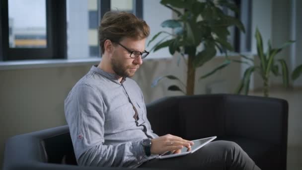 Homme d'affaires assis sur le canapé dans le bureau en utilisant une tablette numérique — Video