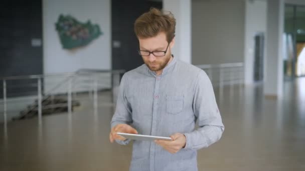 A man walks in waiting room at the Train Station, checks for updates in social networks in the gadjet — Stock video