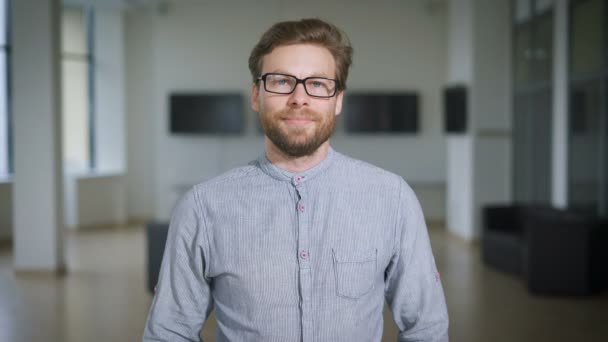 A hallban van egy szőke fiatal férfi szemüveg és kék inget és mosolyogva — Stock videók