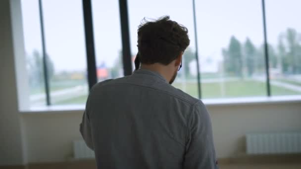 Young man with glasses standing in the room and very upset talking on cell phone. — Stock video