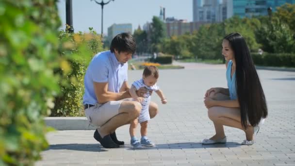 Молоді батьки грають зі своєю дитиною на алеї . — стокове відео