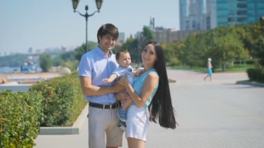 Genç aile sokakta üzerinde dururken kamera bakıyor.