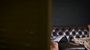 Karnı yavaşça okşayarak ve dergi okuma büyük kahverengi kanepede oturan siyah elbiseli güzel hamile kadın. Kanepede oturan ve dergi okuma gelecekte anne Close-Up.