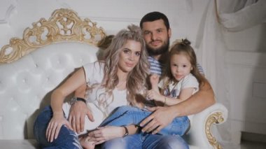 Mutlu aile bekliyor yeni bebeğin kanepede birlikte yakın çekim. Baba, hamile anne ve küçük kızı birlikte birbirlerine sarılma kanepede oturan.