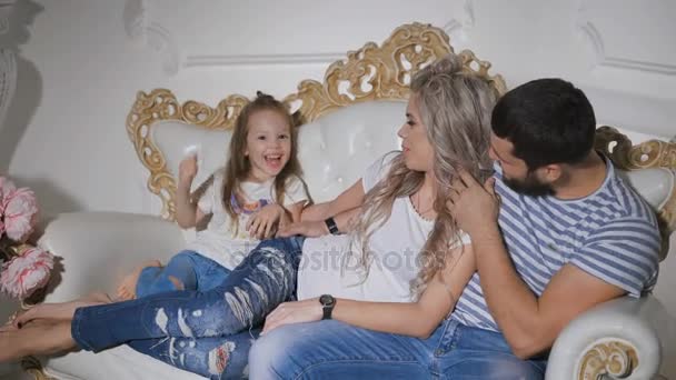 Famiglia felice in attesa di nuovo padre bambino, madre incinta e figlioletta sono seduti insieme sul divano abbracciarsi e sorridere. Piccola ragazza felice sorride, canta — Video Stock