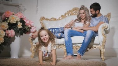 Mutlu bir aile bekliyor yeni bebek, ön planda, gülümseyen kız ile halı üzerinde yalan, surat ve ayakları sarkan. Babası ve hamile anne birlikte oturan