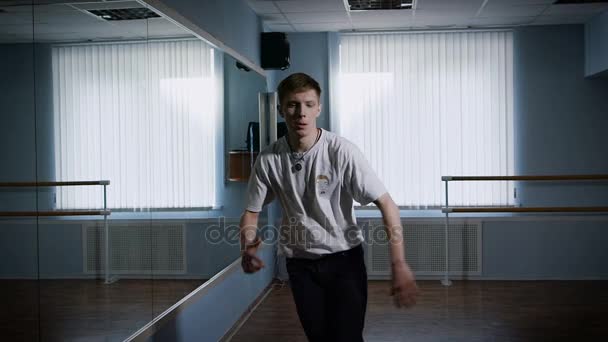 Close up of young hip-hop dancer in black trousers and white shirt performing urban dance standing near the mirror. B-boy is jumping and moving his arms and legs showing freestyle and modern dance. — Stock Video