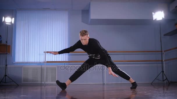Handsome hip-hop dancer dressed in black trousers and pullover performing handstand as an element of urbanstyle and streetdance in the classroom. — Stock Video