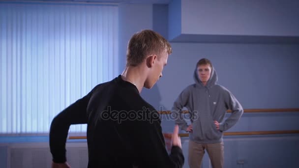 Jonge hip-hop danser in zwarte broek en trui is deelnemen aan breakdance gevecht met zijn vriend. Jongen in het zwart is het uitvoeren van urbanstyle dansen op de kamer. — Stockvideo