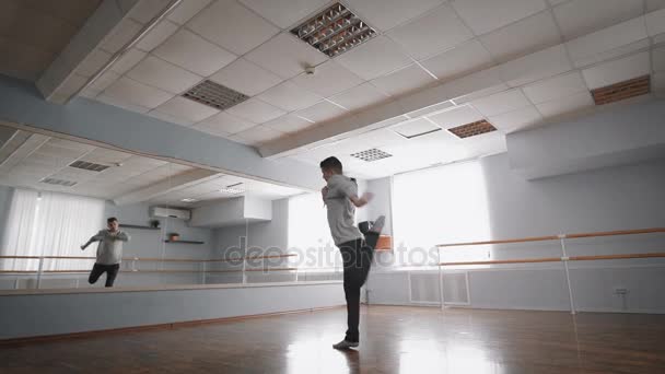 Young man in grey pullover dancing modern dance in the ballroom with barre around. Young flowing man is showing wonderful dancing elements of contemporary dance. Young man making leap — Stock Video