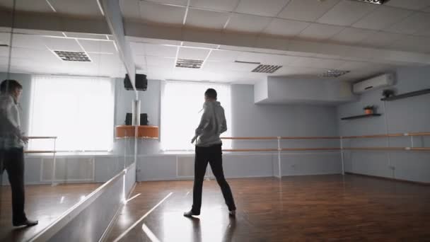 Jonge mooie danseres springen en spinnen in de buurt van de spiegel in de balzaal. Lid van de dansgroep in grijze pullover is in opleiding voor nieuwe jazz moderne dans. — Stockvideo