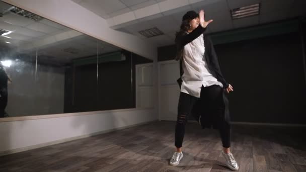 Female dancer in white shirt, black trousers and black cap showing jazz modern dancing. Girl is expressively dancing and professionaly doing elements of streetstyle dance. — Stock Video