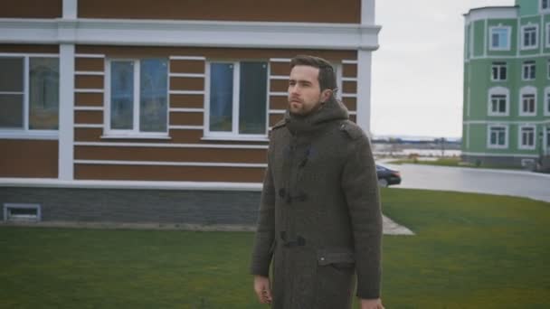 A man in a gray coat in the autumn weather walks on a footpath. Against the background of the city, colorful houses. — Stock Video