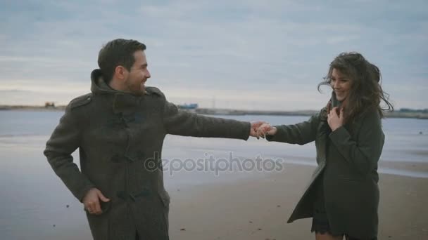 Slunečné počasí na dobrou náladu. Milující pár běží podél vody v písku. Jsou zamilovaní a šťastní. Muž vytáhl jeho přítelkyně ruku a ona běží za ním. — Stock video