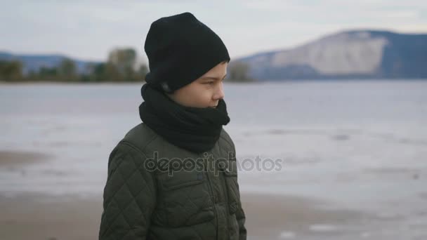 Baywalk. . Chlapec chodí na pláži. Teple oblečen. Na sobě měl světle barevné kalhoty a černé boty. Mladý muž vážné náladu, pomyslel si. — Stock video