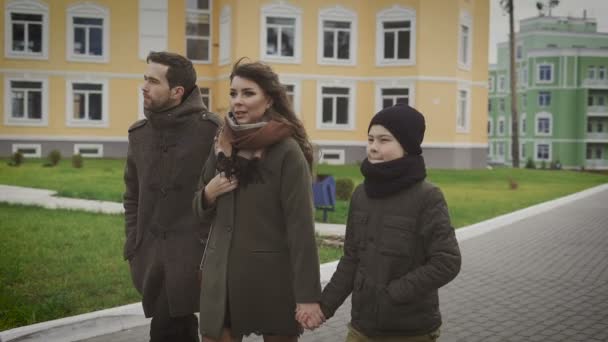 Mutlu aile yürüyüş. Baba, anne ve çocuk. Onlar geziniyor. Güzel kadın Paltonu ve kaşkolünü oğlunun elini tutarak ve hikayesini anlatıyor. — Stok video