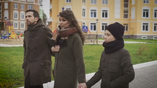 Primer plano de feliz padre, madre e hijo dando un paseo juntos. Familia en ropa de abrigo están caminando juntos en la calle. Padre e hijo están hablando . — Vídeo de stock