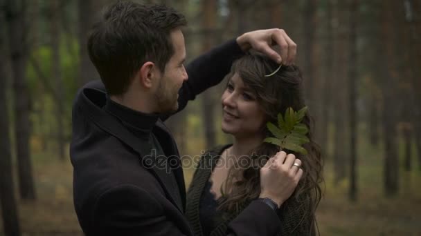 Um casal apaixonado na floresta ao amanhecer. Jovem abraçando sua namorada e brincando com o cabelo dela. Ele estava carregando uma folha verde de uma árvore. eles estão na floresta em um ensolarado para uma sessão de fotos . — Vídeo de Stock