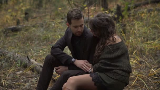 クローズ アップの幸せカップルが森の中にデートします。笑顔の男性と女性は、森の木々 の中のログに座っています。若い男と女お互いを見て. — ストック動画