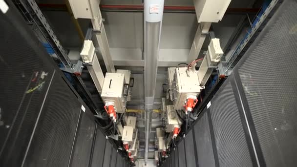 A long series of special cabinets designed for ventilation server on a large industrial plant. Devices connected to a common power supply by cables with red plug. Thin corridor with lamp for lighting. — Stock Video