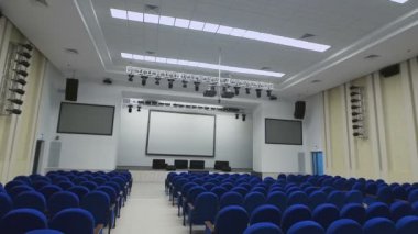 Oturma yeri, ekipman projektör sunular için bol olan ferah, modern konferans salonu. Kamera aşağı koridorda mavi koltuk satırlar arasında taşır..