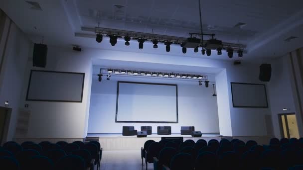 Moderní koncertní sál. Scéna je jasně osvětlena profesionální osvětlovací zařízení. Kamera se pohybuje mezi řadami sedadel a pak stoupá. — Stock video