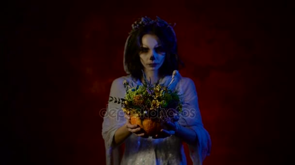 Gros plan d'un bouquet de fleurs entre les mains d'une fille qui regarde la caméra. Jeune belle femme avec maquillage d'art participe à la fête d'Halloween . — Video