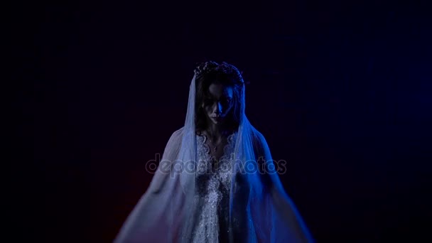Юный призрак невесты поднимает руки вверх, как крылья. Молодая женщина с гирляндой на голове стоит на темном фоне позади нее . — стоковое видео