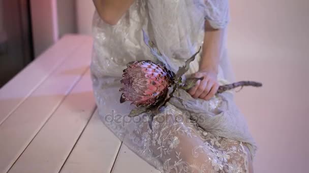 Närbild av en kropp ung flicka i vit brudklänning från hennes knän inför med kreativa skrämmande och läskiga halloween make. utseende som sitter på bänken blomman i händer de letar — Stockvideo