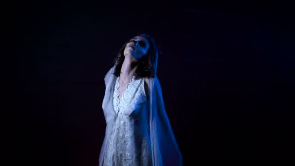 Ghost of young bride in white dress and veil. Moving scarry girl in with halloween make-up is standing against black background. Mysterious womanin horror behind . — Stock Video