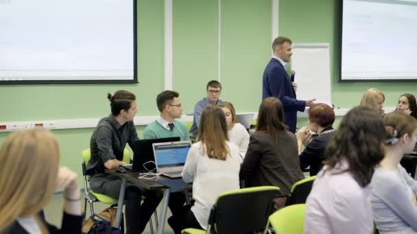 Gruppo di studenti in classe presso l'università stanno ascoltando con attenzione la lezione di Economia del famoso docente. Speaker in tuta blu con il microfono è molto positivo e consegna — Video Stock