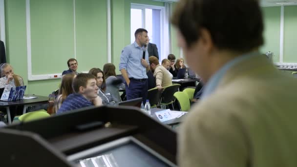 Man met een microfoon is het bezit van een zakelijke bijeenkomst. Publiek wordt gevuld door managers uit verschillende branches en bedrijven. Man op de voorgrond, besturingselementen de computer ontworpen voor conferenties. — Stockvideo