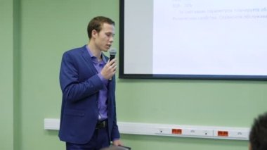 İş Okulu öğrenci Finans için bir seminerde konuşuyor. Genç adam bir mikrofon ve bir tasarı için yaptığı konuşmada kullanır. Öğrenci elinde bir tablet kağıtları ile tutuyor..