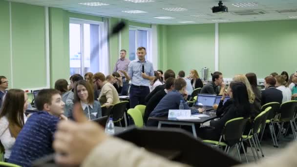 Young teacher in blue shirt with the microphone in his hands explaining rules and task of business gaming simulation to his students in classroom at the university. — Stock Video