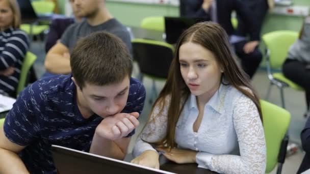 Tým studentů o praktické školení v učebně. Dívka vysvětluje svým přátelům podstatu úkolu, ukazuje příklad obrazovky přenosného počítače. — Stock video