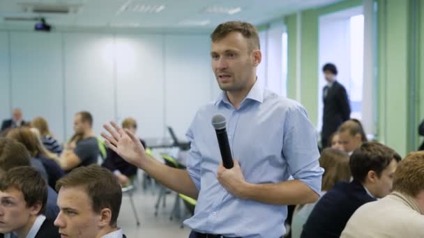 Conférencier de renom parle lors d'une conférence d'affaires devant un gestionnaire de salle complète. Les participants écoutent attentivement le conférencier. Jeune homme parle dans un micro et gestuelle avec ses mains . — Video