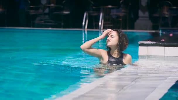 Şirin kız havuzda ayakta ve saç düzeltiyor ve uzakta yüzen. Genç kadın tatilde aktif vaktini geçiriyor. — Stok video