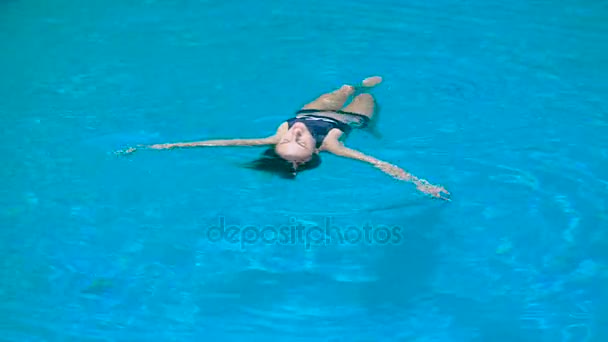 Mujer en forma adorable en traje de baño negro es relajante luying en el agua. Joven chica bien formada está mostrando comodidad y placer flotando en la piscina . — Vídeo de stock