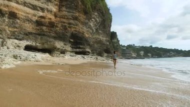 Genç ince esmer deniz kıyısı yürüyüş ve denize bakarak. Güzel manken suda geziniyor rock yakınındaki Balinese sahilde poz.
