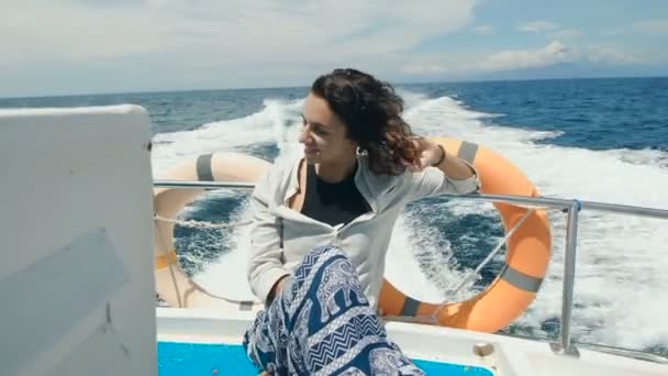 Young beautiful female traveler in casual clothing is having cruise on board of a yacht at the open sea. Happy woman is rising her hands and enjoying the wind streaming her hair and touching her face. — Stock Video