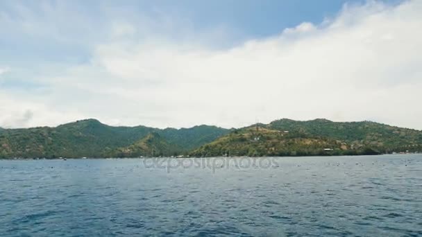 Een uitzicht op de blauwe zee met kleine golven en een eiland met veel bomen en groen gras de hemel is blauw en wolken is wit — Stockvideo