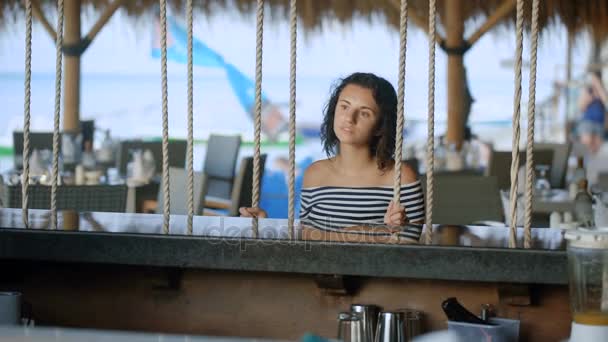 Jolie brune assise au bar créatif du complexe hôtelier. Restaurant utilisant balançoire au lieu des chaises. Jeune femme avec de beaux yeux regarde au loin . — Video