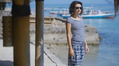 Güzel esmer okyanus somut bir iskelede gitti. Genç kadın saçları ve kıyıda duran güneş gözlüğü düzeltiyor. Resort mesafe içine kız görünüyor.