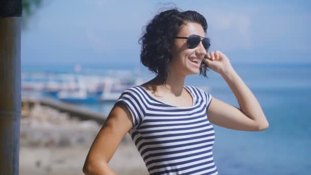 Nahaufnahme einer schönen Brünette mit kurzen krauses Haar mit blauem Meer im Hintergrund an einem sonnigen Sommertag. junges hübsches Mädchen posiert und lächelt am Strand von Bali Island. — Stockvideo
