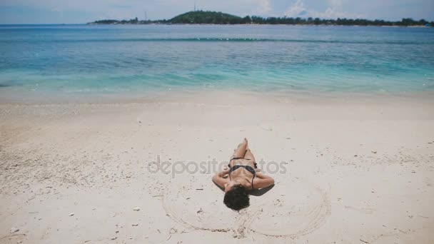 Der strand auf der insel bali. Mädchen in schwarzem Badeanzug liegt an einem Sandstrand und ruht sich aus. sein beruhigender Sand, sonnige, saubere und türkisfarbene Ozeaninsel. — Stockvideo