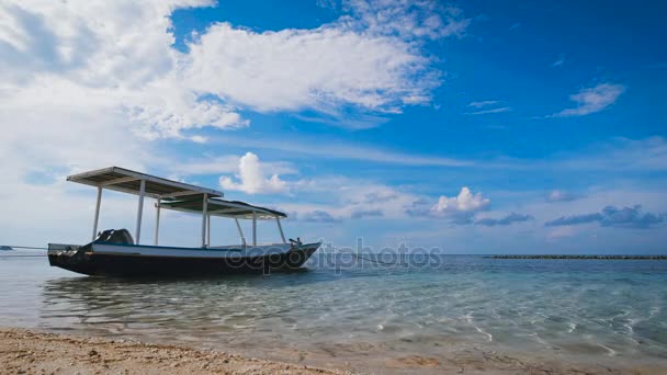 Small boat with a roof standing next to a sandy beach in the open ocean, where there are small waves — Stock Video