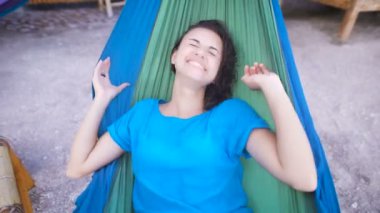 Tropik sahilde hamakta yatan, yüzünü gizleme ve mutlu bir şekilde gülerek neşeli kız. Mavi elbiseli güzel kadın gülümseyerek ve doku hızıyla ithe bar Bali adasında rahatlatıcı.