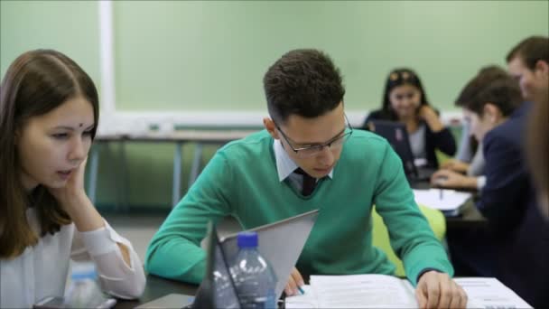 Étudiants à la leçon d'économie à l'université. Homme étudiant attentivement le matériel de cours et la fille à côté de lui travaillant sur un ordinateur portable. Processus éducatif des futurs financiers . — Video